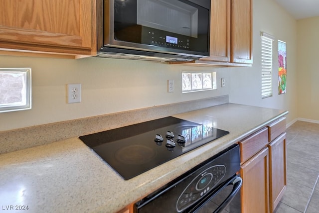 kitchen featuring black appliances, light stone counters, and light tile patterned floors