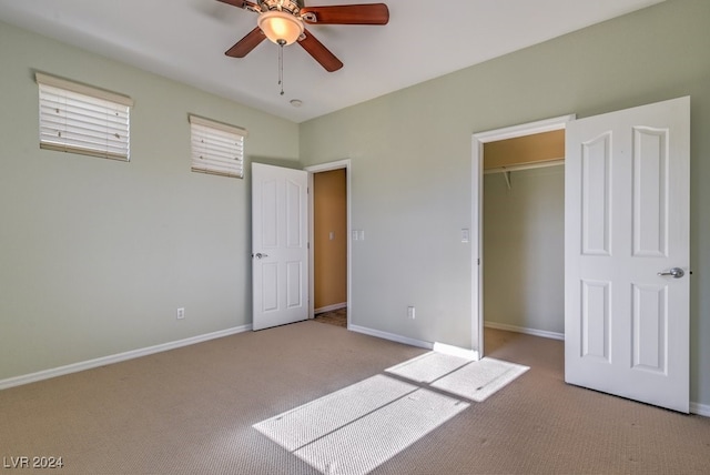 unfurnished bedroom featuring a closet, a walk in closet, light carpet, and ceiling fan