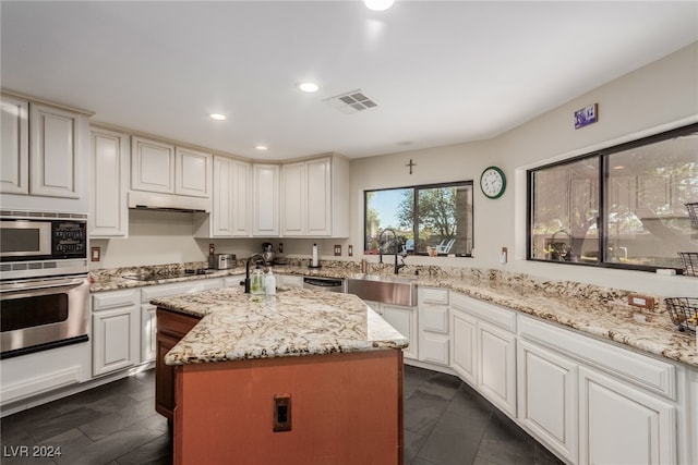 kitchen with white cabinetry, light stone countertops, a center island, stainless steel appliances, and sink