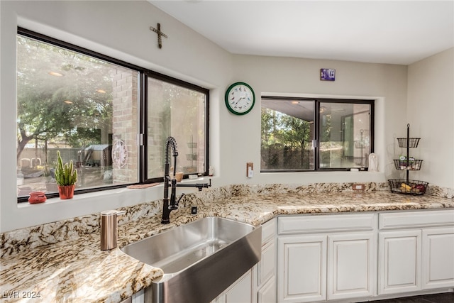 kitchen featuring light stone countertops, white cabinetry, and sink