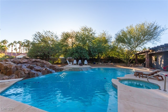 pool at dusk with an in ground hot tub, pool water feature, and a patio area