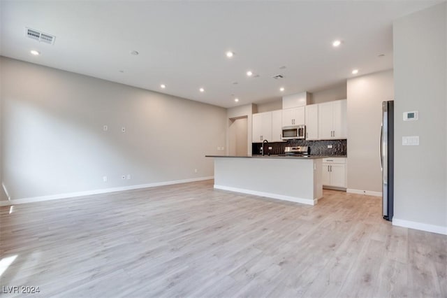 kitchen with white cabinetry, light hardwood / wood-style flooring, a center island with sink, appliances with stainless steel finishes, and backsplash