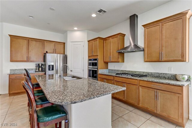 kitchen featuring appliances with stainless steel finishes, an island with sink, sink, a kitchen bar, and wall chimney range hood