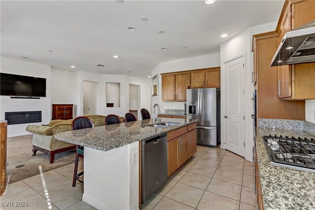 kitchen featuring a breakfast bar, sink, an island with sink, stainless steel appliances, and exhaust hood