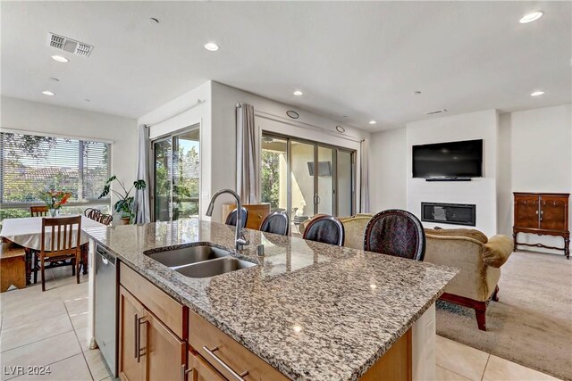 kitchen with sink, light stone counters, light tile patterned floors, dishwasher, and an island with sink