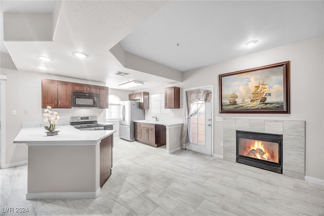 kitchen featuring kitchen peninsula, black appliances, a textured ceiling, sink, and a fireplace