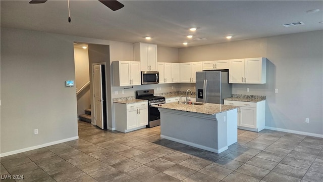 kitchen featuring appliances with stainless steel finishes, light stone counters, sink, a center island with sink, and white cabinets