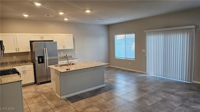 kitchen featuring white cabinets, sink, stainless steel refrigerator with ice dispenser, an island with sink, and light stone counters