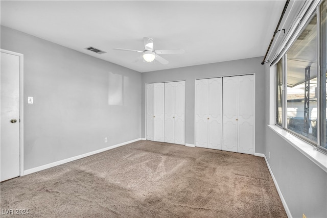 unfurnished bedroom featuring ceiling fan, multiple closets, and carpet floors