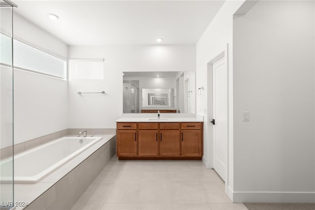 bathroom with a relaxing tiled tub, vanity, and tile patterned floors