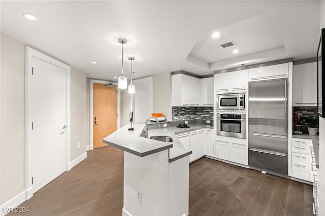 kitchen featuring visible vents, a sink, dark wood finished floors, a peninsula, and built in appliances