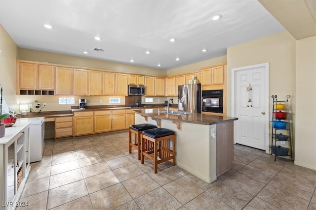 kitchen featuring a breakfast bar area, light brown cabinetry, a center island with sink, and stainless steel appliances