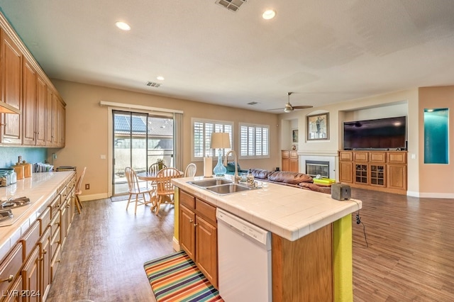 kitchen featuring dishwasher, a center island with sink, sink, light wood-type flooring, and tile counters