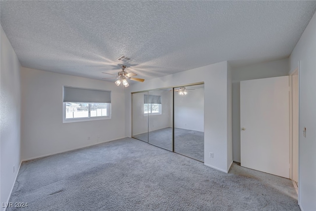 unfurnished bedroom featuring a closet, a textured ceiling, light colored carpet, and ceiling fan