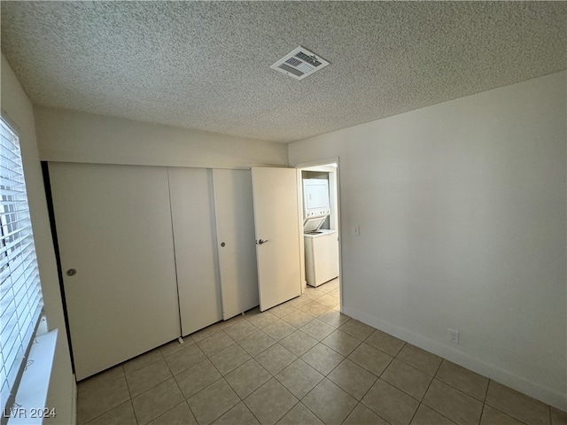 unfurnished bedroom featuring light tile patterned floors, washer / dryer, a textured ceiling, and a closet