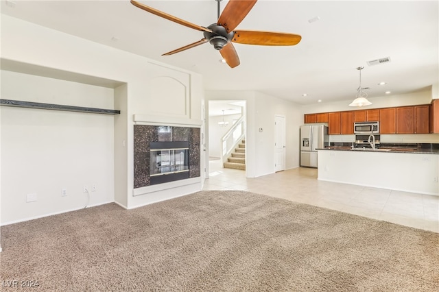 unfurnished living room featuring light carpet, sink, ceiling fan, and a premium fireplace