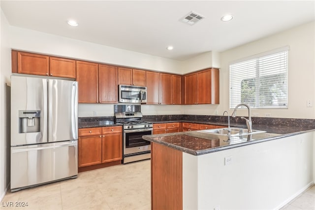 kitchen featuring kitchen peninsula, stainless steel appliances, sink, light tile patterned floors, and dark stone countertops