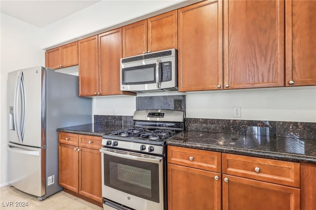 kitchen with appliances with stainless steel finishes, dark stone counters, and light tile patterned flooring