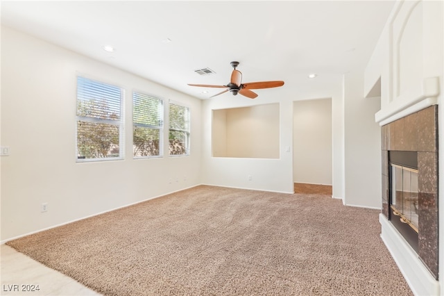 unfurnished living room with ceiling fan, light colored carpet, and a tile fireplace