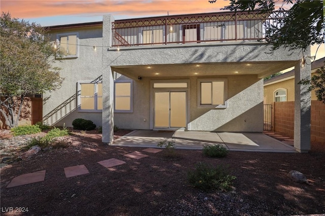 back house at dusk with a balcony and a patio area