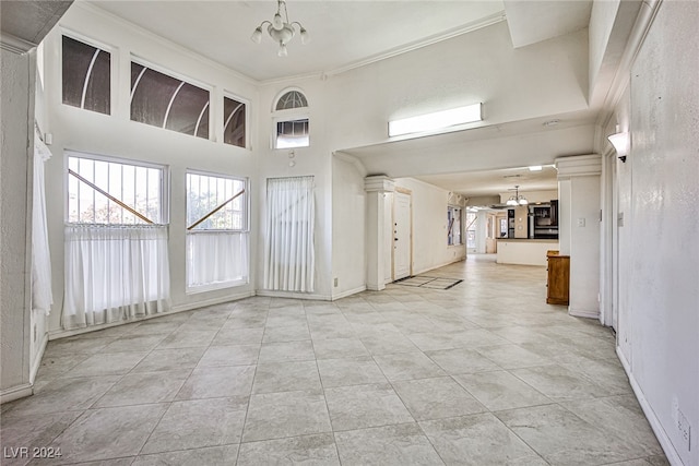 interior space with light tile patterned flooring, ornamental molding, a towering ceiling, a chandelier, and decorative columns