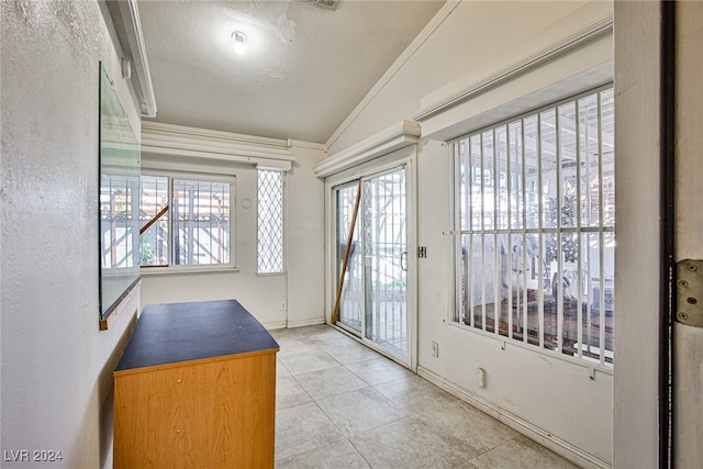 doorway featuring lofted ceiling, a textured ceiling, light tile patterned floors, and ornamental molding