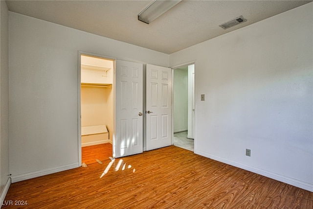 unfurnished bedroom featuring hardwood / wood-style floors, a walk in closet, and a closet