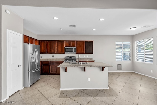 kitchen featuring appliances with stainless steel finishes, light tile patterned floors, sink, a breakfast bar, and a kitchen island with sink