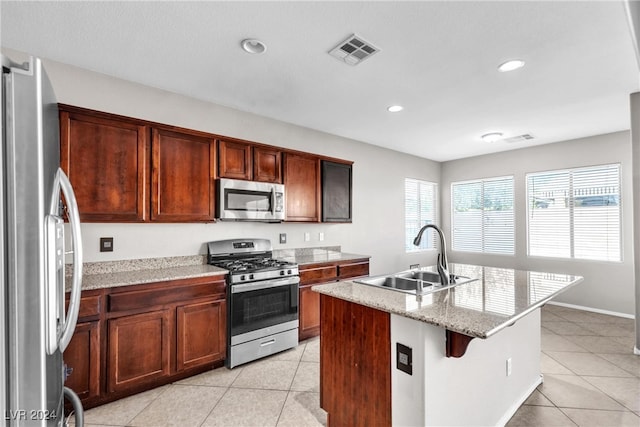 kitchen with sink, a breakfast bar area, an island with sink, light tile patterned floors, and appliances with stainless steel finishes