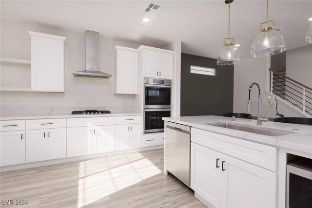 kitchen with appliances with stainless steel finishes, wall chimney exhaust hood, white cabinets, and light stone countertops