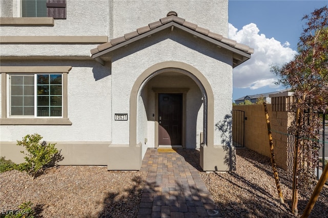 entrance to property with a tile roof, fence, and stucco siding