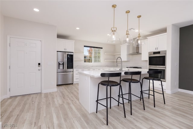 kitchen with stainless steel appliances, white cabinetry, sink, an island with sink, and wall chimney exhaust hood