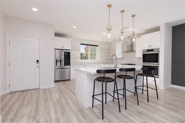 kitchen featuring wall chimney exhaust hood, stainless steel appliances, light countertops, white cabinetry, and a sink