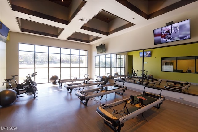 exercise room with a towering ceiling, coffered ceiling, and wood finished floors