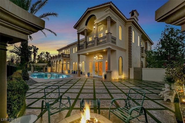 back house at dusk featuring a patio, a balcony, and an outdoor fire pit