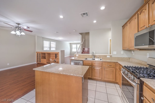 kitchen featuring light stone counters, stainless steel appliances, a kitchen island, sink, and light hardwood / wood-style flooring