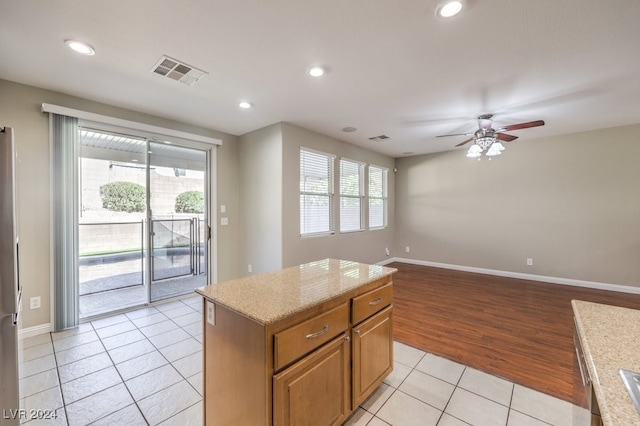 kitchen featuring light hardwood / wood-style floors, ceiling fan, light stone counters, and a kitchen island