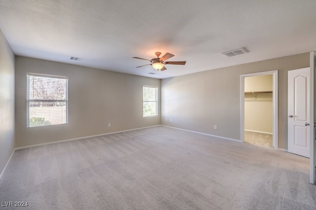 unfurnished bedroom featuring a textured ceiling, light carpet, ceiling fan, a closet, and a spacious closet