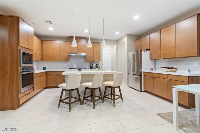 kitchen featuring sink, stainless steel appliances, decorative light fixtures, a breakfast bar area, and a center island with sink