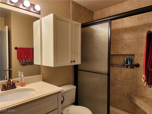 bathroom with toilet, vanity, and a shower with shower door