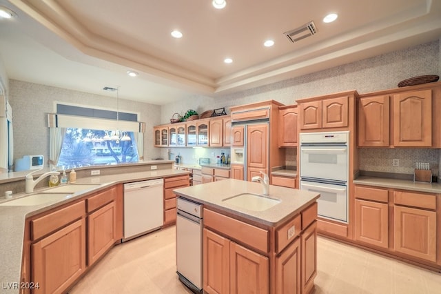 kitchen with a center island with sink, hanging light fixtures, sink, a tray ceiling, and white appliances