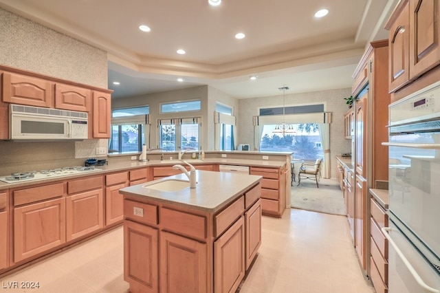 kitchen featuring a chandelier, sink, an island with sink, pendant lighting, and white appliances