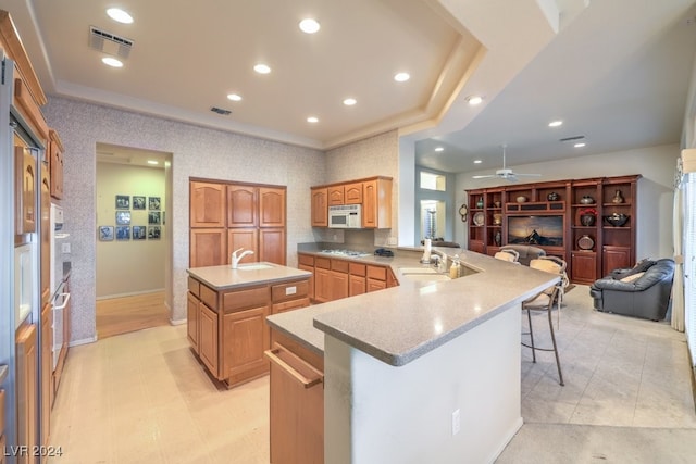 kitchen featuring a center island with sink, appliances with stainless steel finishes, a breakfast bar, kitchen peninsula, and ceiling fan