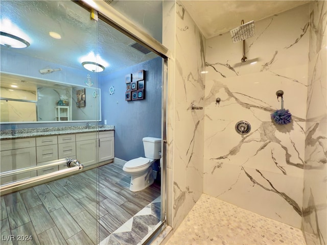 bathroom with hardwood / wood-style flooring, vanity, toilet, and tiled shower