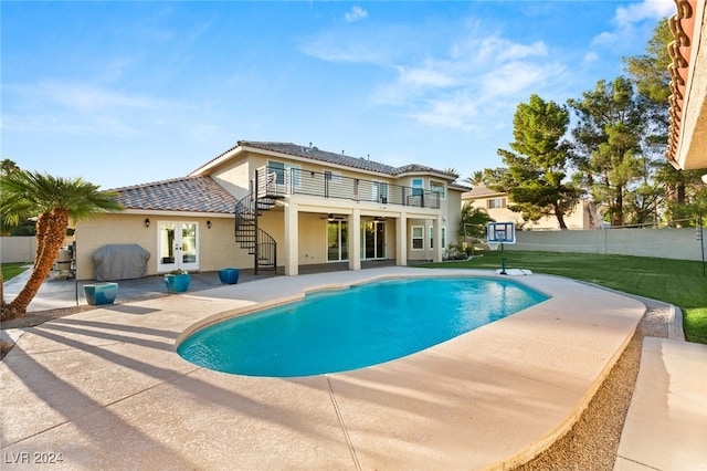 rear view of house with french doors, a fenced in pool, a balcony, a patio area, and a yard