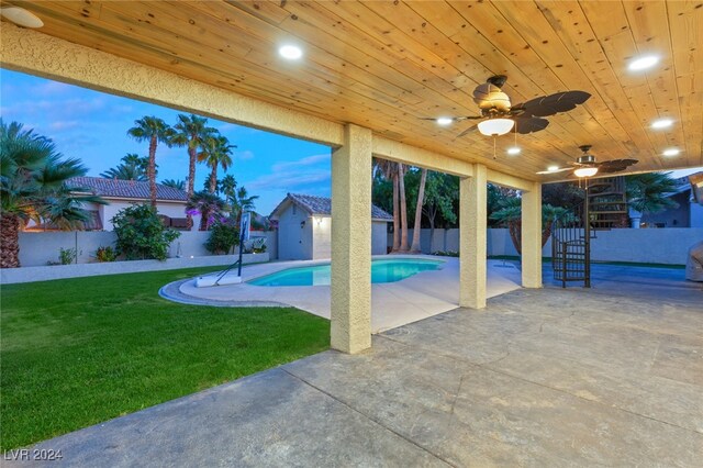 pool at dusk featuring ceiling fan, a yard, and a patio area