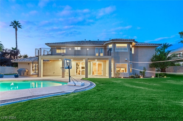 back house at dusk with a patio area, a lawn, and a balcony