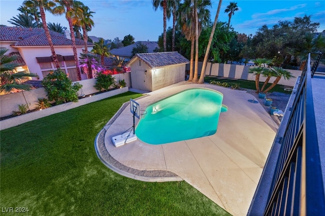 pool at dusk featuring a patio, a yard, and a storage shed