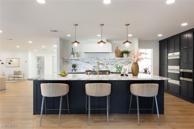 kitchen featuring a kitchen breakfast bar, light hardwood / wood-style flooring, hanging light fixtures, and light stone counters