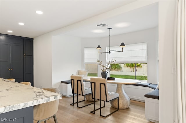 interior space featuring a breakfast bar area, pendant lighting, light stone counters, and light hardwood / wood-style flooring